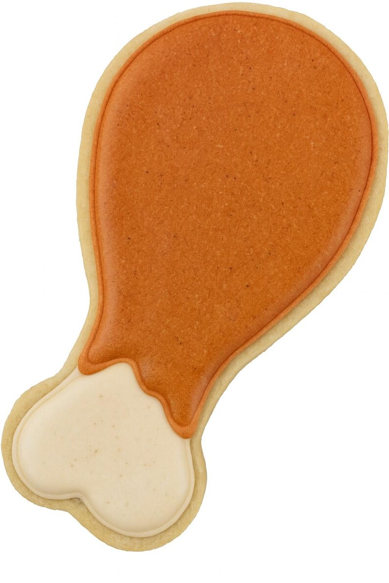 May include: A decorated cookie in the shape of a turkey leg. The cookie has a light tan border, with a textured orange-brown top and a cream-colored bottom, resembling the meat and bone of a cooked turkey leg.
