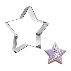 May include: A stainless steel star-shaped cookie cutter next to a decorated star-shaped cookie. The cookie has a lavender-colored icing with white floral design and a golden-brown edge. The cutter is made of shiny, silver-colored metal.