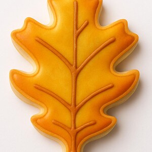 May include: A leaf-shaped cookie with a golden yellow center and a darker orange outline and vein details. The cookie is a fall-themed treat, perfect for autumn celebrations and gatherings. The cookie is a delicious and decorative dessert.