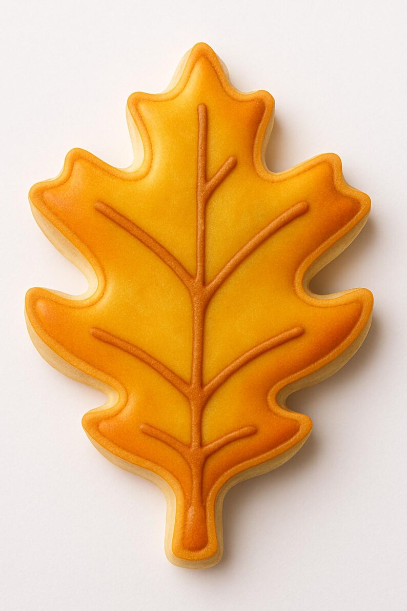 May include: A leaf-shaped cookie with a golden yellow center and a darker orange outline and vein details. The cookie is a fall-themed treat, perfect for autumn celebrations and gatherings. The cookie is a delicious and decorative dessert.