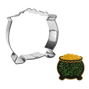 May include: A silver-colored metal cookie cutter in the shape of a cauldron, next to a decorated cookie. The cookie is black with green floral designs and gold coins.