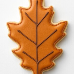 May include: A leaf-shaped cookie with orange icing and brown vein details. The cookie has a light brown outline and a white background. This autumn-themed treat is perfect for fall celebrations.