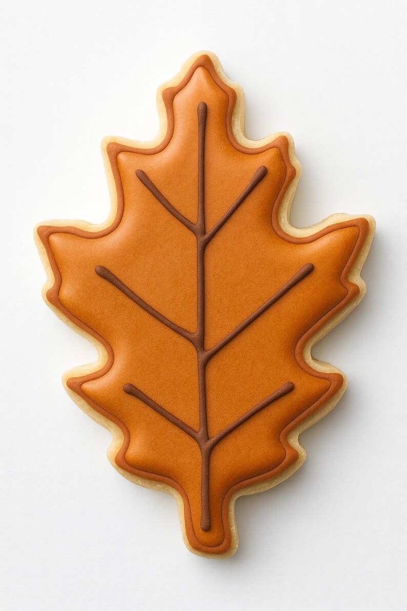 May include: A leaf-shaped cookie with orange icing and brown vein details. The cookie has a light brown outline and a white background. This autumn-themed treat is perfect for fall celebrations.