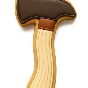 May include: An axe-shaped biscuit. The axe head is dark brown, the handle is light brown with vertical lines, and the outline is a light tan colour. The biscuit is set against a white background.