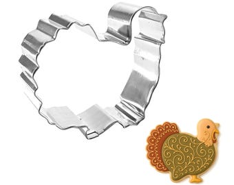 May include: A shiny, silver-colored turkey-shaped cookie cutter with a crimped edge. Next to it is a decorative turkey-shaped cookie with a brown, orange, and yellow design. Perfect for Thanksgiving or fall baking.