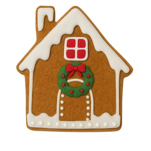 May include: A gingerbread house cookie shaped like a cottage with brown dough, white icing trim resembling snow on the roof and base, a red window, and a green wreath with a red bow centered above a doorway outlined with white icing dots.