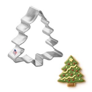 May include: A silver-colored Christmas tree cookie cutter with a wavy edge, next to a decorated Christmas tree cookie. The cookie is green with red and yellow decorations. The cookie cutter has a small "Made in the USA" stamp.