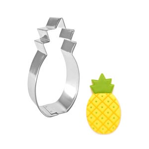 May include: A shiny, silver pineapple-shaped cookie cutter next to a decorated pineapple cookie. The cookie is yellow with a green top and a grid pattern. The cookie cutter is made of metal.