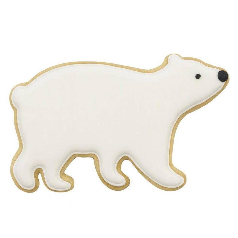 May include: A polar bear cookie with white icing and a golden-brown cookie base. The bear has black eyes and a black nose. The cookie is in the shape of a walking polar bear.