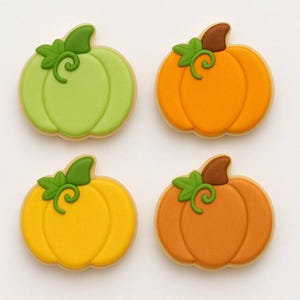 May include: Four pumpkin-shaped cookies with green, orange, yellow, and brown icing. Each cookie has a green leaf and stem design. The cookies are on a white surface.