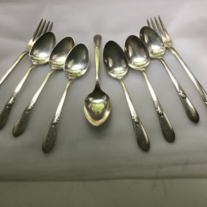 May include: A set of eight silver-plated spoons and forks with ornate handles. The spoons have a rounded bowl shape and the forks have three tines.