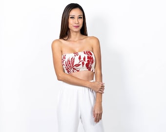 May include: A woman wearing a white strapless top with red floral print and white wide-leg pants. She is standing on a white background.