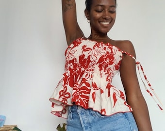Könnte beinhalten: Eine Frau trägt ein rotes und weißes, blumiges Crop-Top mit Rüschen am Saum und Jeans-Shorts.