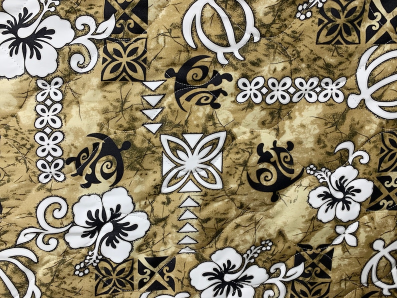 Op de afbeelding: Een bruine stof met een wit en zwart Hawaiiaans print met hibiscus bloemen, schildpadontwerpen en geometrische patronen.
