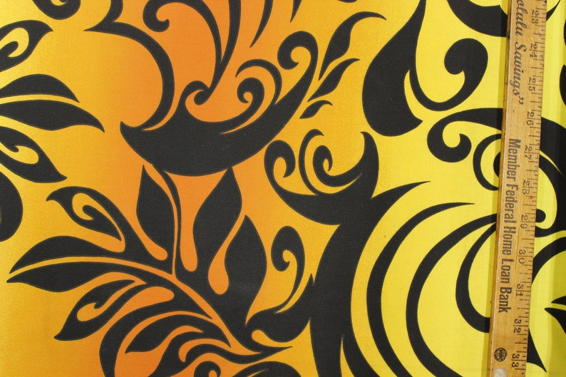 May include: A yellow and orange fabric with a black floral pattern. The fabric has a gradient from orange to yellow. The pattern is made up of swirls and leaves.
