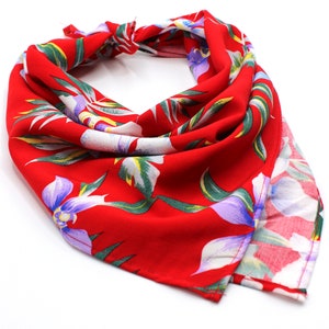 May include: A red bandana with a floral print featuring white, green, and purple flowers. The bandana is folded and tied in a knot.