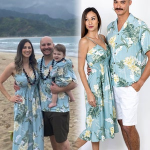 Pu&ograve; includere: Una famiglia di quattro persone che indossano camicie e abiti coordinati con stampa floreale blu e verde. Gli adulti tengono un bambino in un outfit abbinato. La famiglia &egrave; in piedi su una spiaggia con una catena montuosa sullo sfondo.