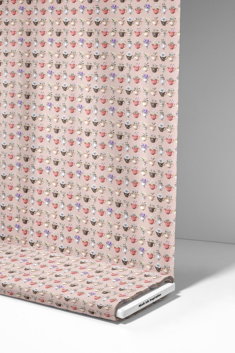 May include: A fabric roll displaying a repeating pattern of teacups filled with flowers on a pale pink backdrop. The teacups are in various colours, including red, brown, and white. The fabric is printed with a floral design.