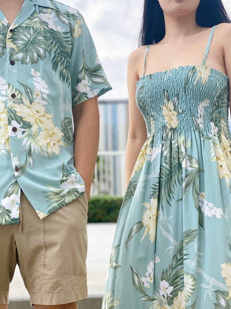 May include: A matching set of light blue tropical print clothing. The shirt has a button-up front and short sleeves. The dress has a spaghetti strap design and a gathered bodice.