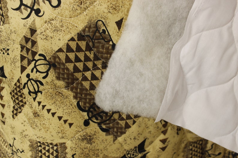 May include: Close-up of a white quilted fabric with a brown and tan patterned fabric underneath. The white fabric has a fluffy texture and the patterned fabric has a geometric design.