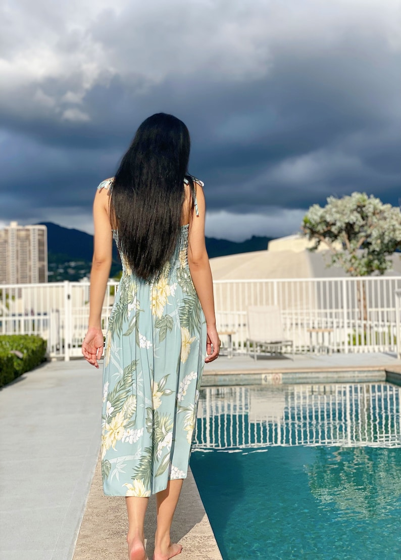 May include: A woman with long black hair walks towards a swimming pool wearing a light blue floral maxi dress.