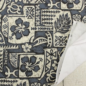 May include: A close-up of a blue and white patterned fabric with a Hawaiian theme. The fabric features hibiscus flowers, geometric designs, and a cracked, textured background.