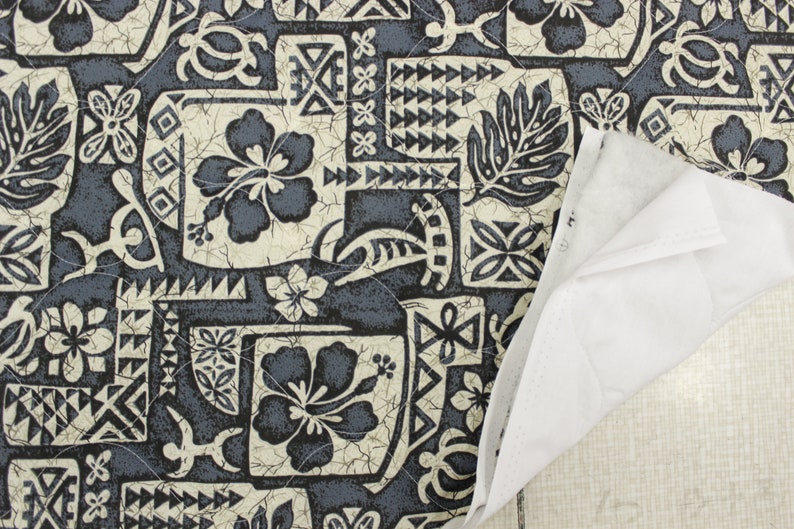 May include: A close-up of a blue and white patterned fabric with a Hawaiian theme. The fabric features hibiscus flowers, geometric designs, and a cracked, textured background.
