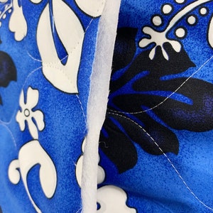 May include: Close-up of a blue fabric with a white and black floral pattern. The fabric is quilted and has a white seam running down the center.