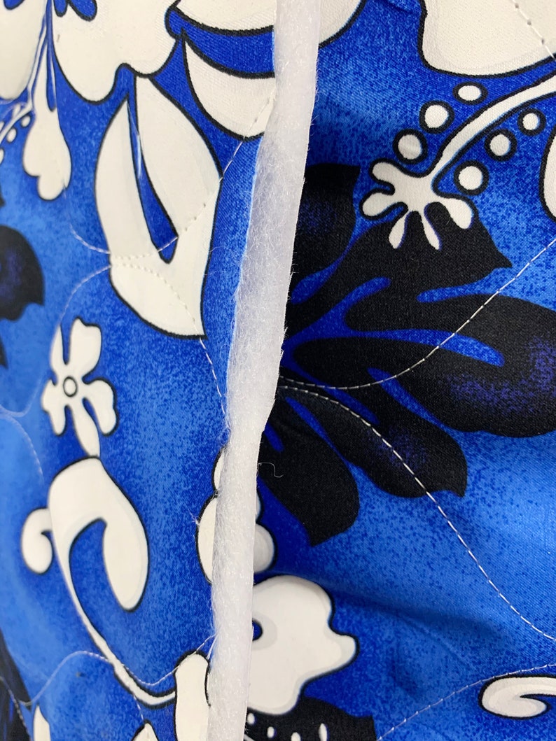May include: Close-up of a blue fabric with a white and black floral pattern. The fabric is quilted and has a white seam running down the center.