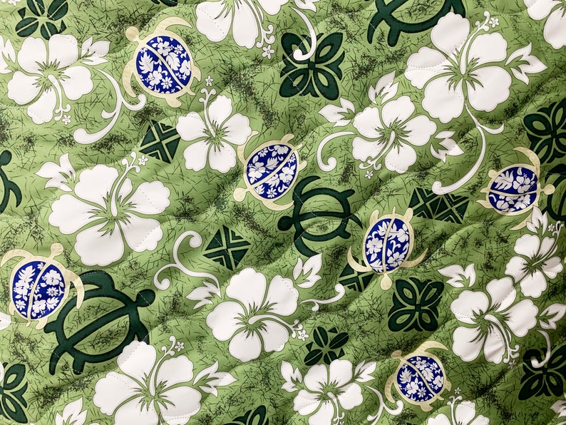 May include: Green fabric with a repeating pattern of white hibiscus flowers, green turtles with blue shells, and green stylized floral designs.
