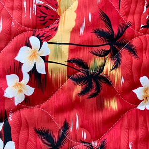 May include: Red fabric with a tropical print featuring palm trees, white flowers, and a sunset scene. The fabric has a quilted texture.