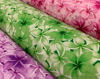 May include: Four rolls of fabric with a floral print. The fabric is in shades of pink, green, purple, and blue. The flowers are a white plumeria design.