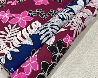 May include: Two rolls of fabric with a tropical floral print. One roll is a dark red fabric with white and pink flowers and leaves. The other roll is a dark blue fabric with white flowers and leaves.