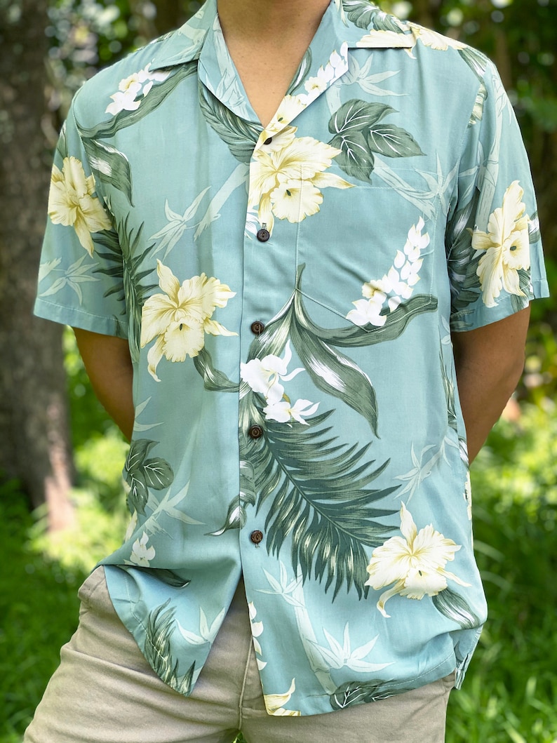 May include: A light blue short-sleeved shirt with a floral print featuring white and yellow flowers and green leaves.