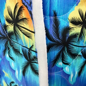 May include: Close-up of a blue and yellow fabric with a palm tree print. The fabric is quilted and has a white seam down the centre.