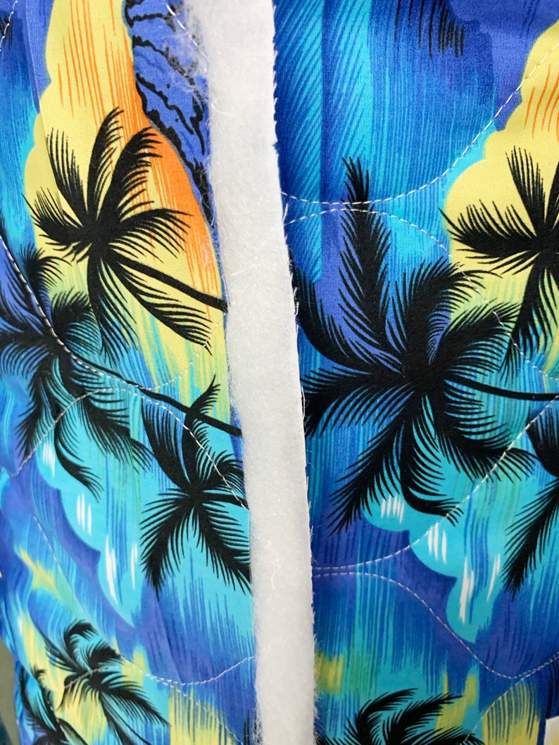 May include: Close-up of a blue and yellow fabric with a palm tree print. The fabric is quilted and has a white seam down the centre.