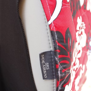 May include: Close-up of a black car seat cover with a red and white floral pattern. The cover has a label that reads "SRS SIDE AIRBAG".