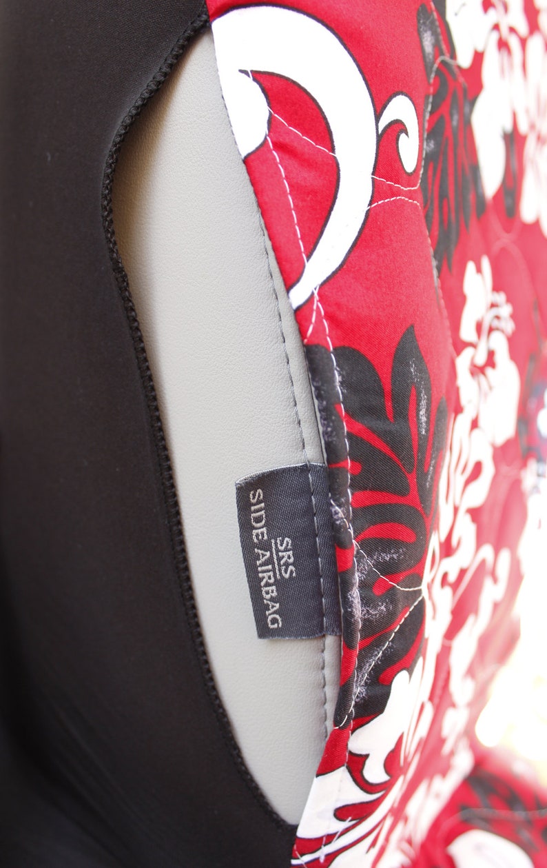 May include: Close-up of a black car seat cover with a red and white floral pattern. The cover has a label that reads "SRS SIDE AIRBAG".