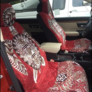 May include: Two red car seat covers with a brown and white patterned design featuring a turtle. The pattern is a traditional Polynesian design.