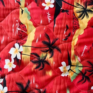 May include: Red fabric with a quilted pattern featuring a tropical print of palm trees, white flowers, and the words "Aloha" and "Hawaii".