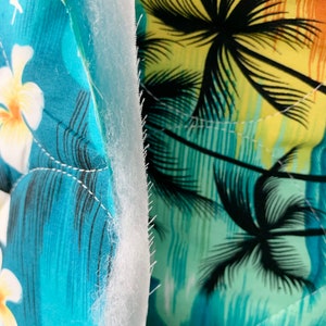 May include: Close-up of a blue and green fabric with a palm tree print. The fabric is layered with a white batting material.