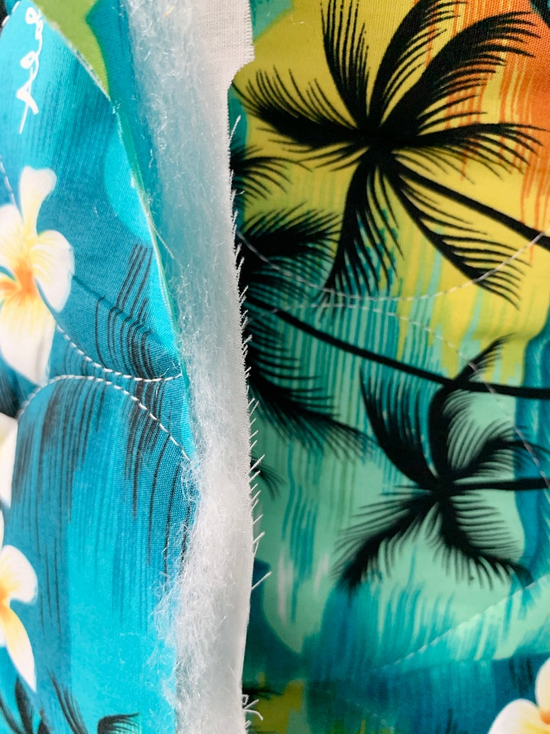 May include: Close-up of a blue and green fabric with a palm tree print. The fabric is layered with a white batting material.