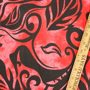 May include: Red fabric with a black floral pattern. The fabric has a distressed look and a ruler is partially visible in the bottom right corner. The ruler has the text "Honolulu Says Measure Your Success By Inches".
