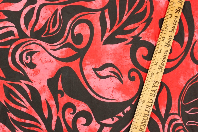 May include: Red fabric with a black floral pattern. The fabric has a distressed look and a ruler is partially visible in the bottom right corner. The ruler has the text "Honolulu Says Measure Your Success By Inches".