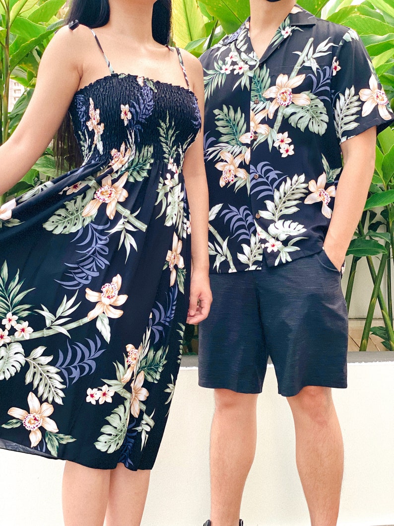 K&ouml;nnte beinhalten: Ein schwarzes und wei&szlig;es Kleid mit Blumenmuster und ein passendes Hemd. Das Kleid hat ein tr&auml;gerloses Design mit einem gerafften Oberteil und einem flie&szlig;enden Rock. Das Hemd hat kurze &Auml;rmel und einen Kragen.