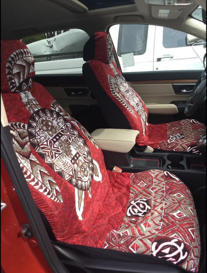 May include: Two red car seat covers with a brown and white patterned design featuring a turtle. The pattern is a traditional Polynesian design.