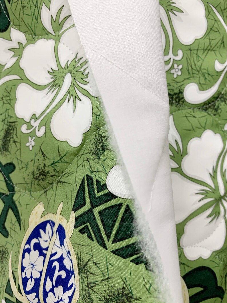 May include: Close-up of a green and white fabric with a floral pattern. The fabric is quilted and has a white backing.
