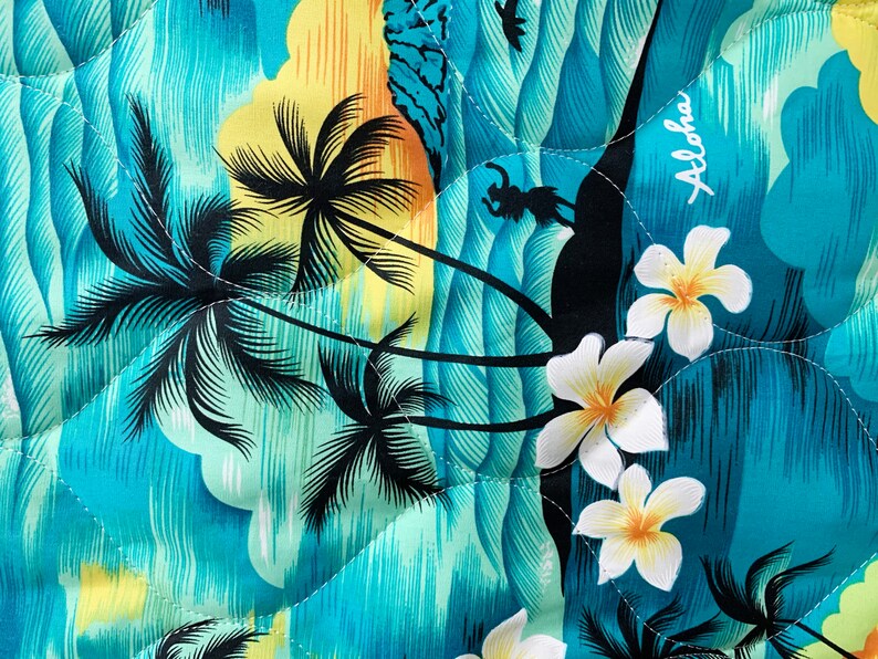 May include: A blue and yellow fabric with a tropical print featuring palm trees, waves, and flowers. The fabric has the word "Aloha" printed on it.