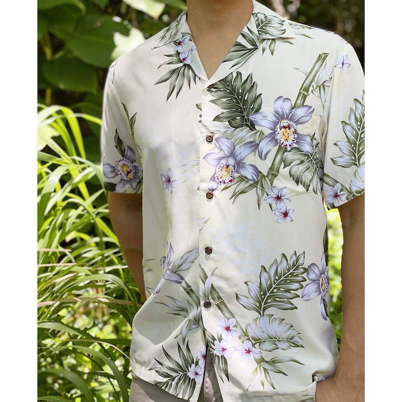 K&ouml;nnte beinhalten: Ein wei&szlig;es, kurz&auml;rmeliges Hemd mit Kn&ouml;pfen und einem Blumendruck mit Orchideen und Bl&auml;ttern. Das Hemd hat eine lockere Passform und einen Kragen.