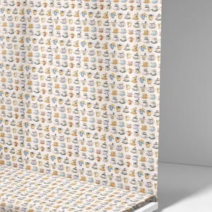 May include: Fabric roll with a cream background, covered in a repeating pattern of watercolour teacups and saucers. The design includes floral details. The text "Ninth Isle Inspiration" is visible on the edge of the roll.